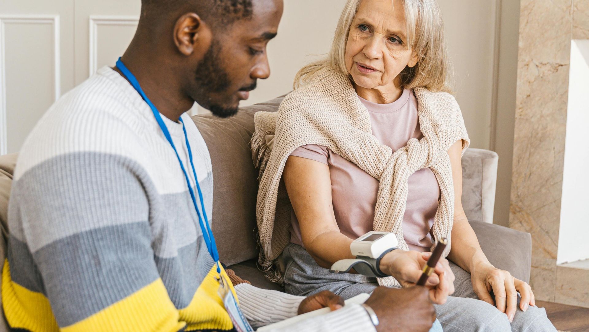 A caring volunteer assists an elderly woman in monitoring her blood pressure indoors.