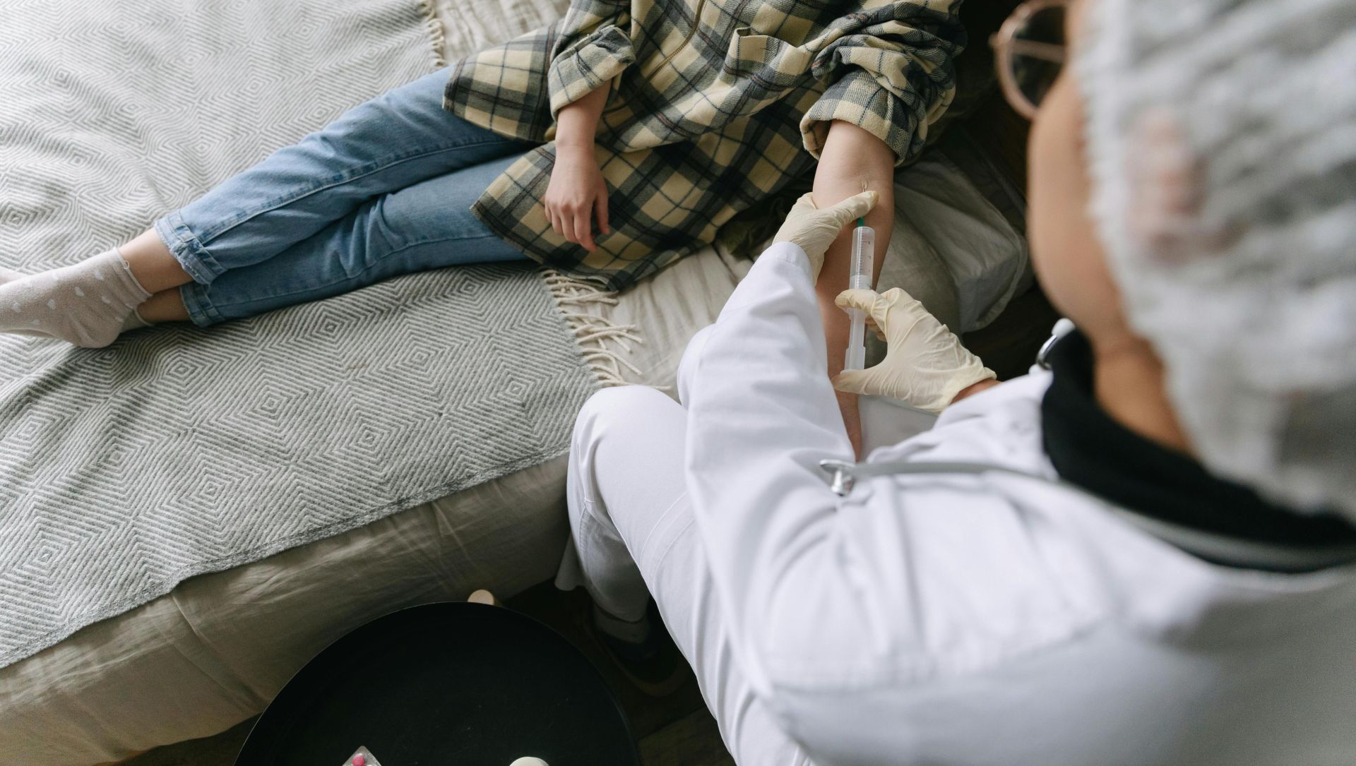 A healthcare professional carefully administers an injection to a patient sitting on a sofa in a cozy room.